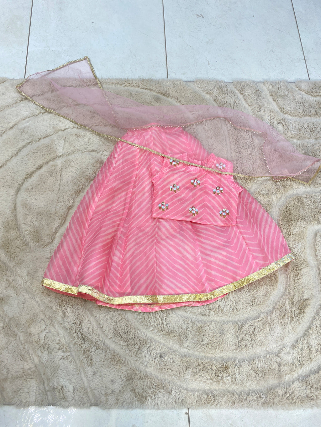 Baby pink lehenga set for girls with intricate Leheriya pattern and embellishments on a soft background.